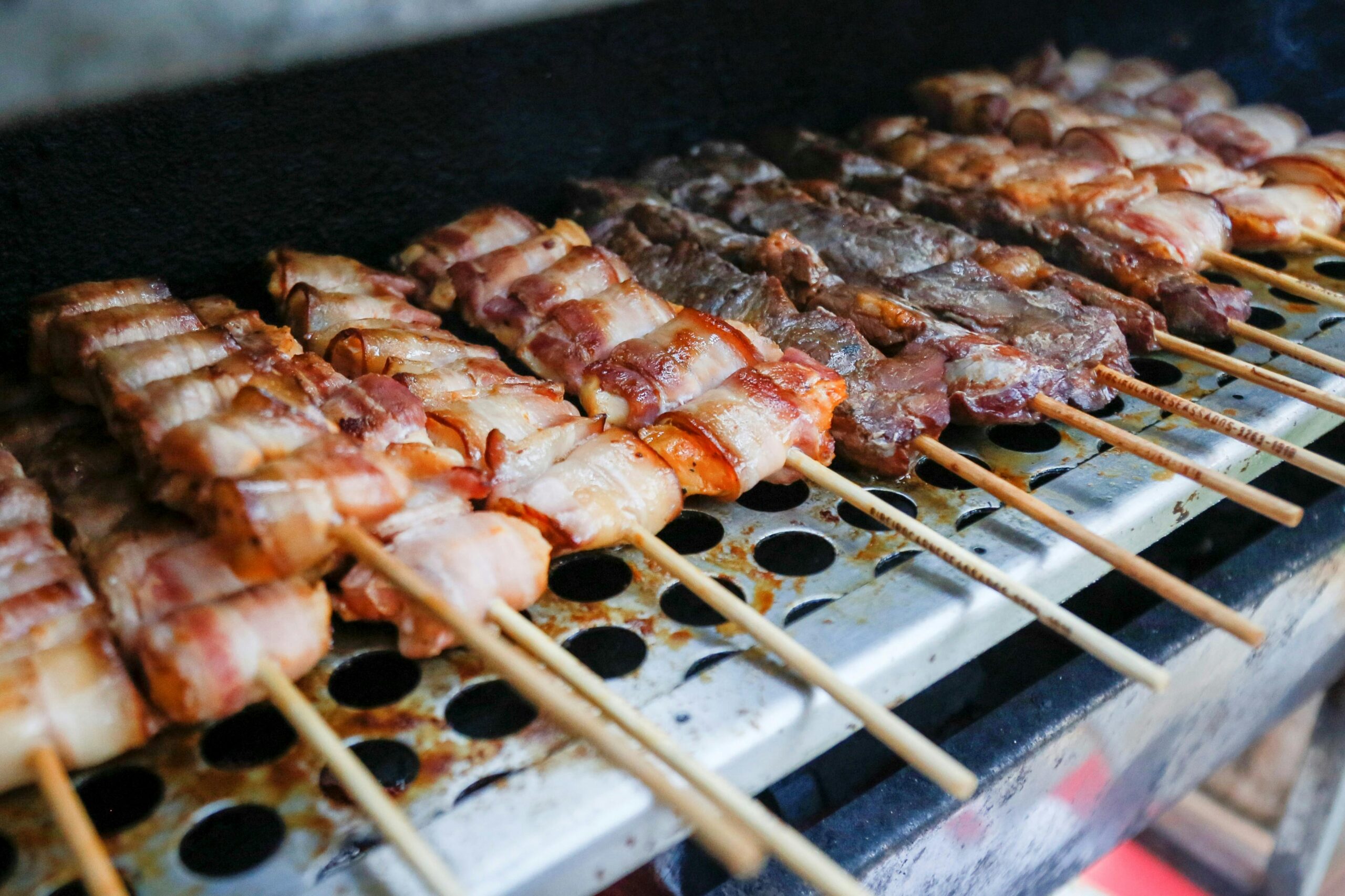 Close-up of various meats on skewers grilling, showcasing a delicious barbecue scene.