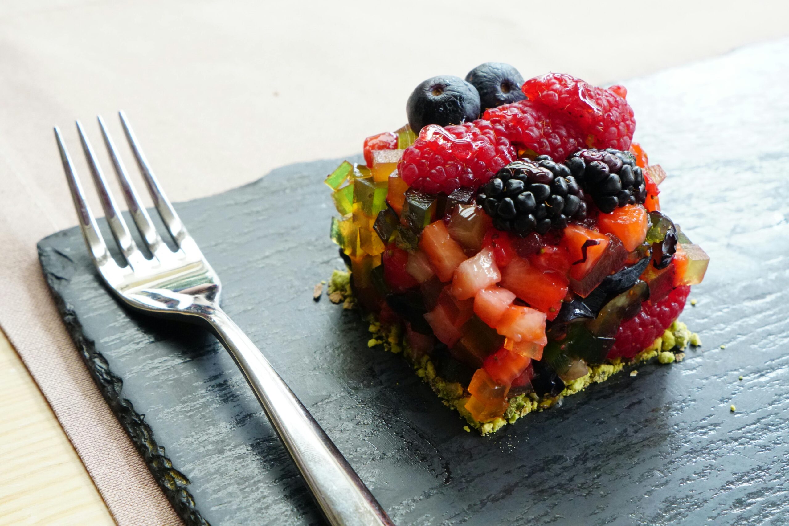 A vibrant mixed berry dessert featuring raspberries, blackberries, and blueberries served elegantly on a slate plate with a fork.