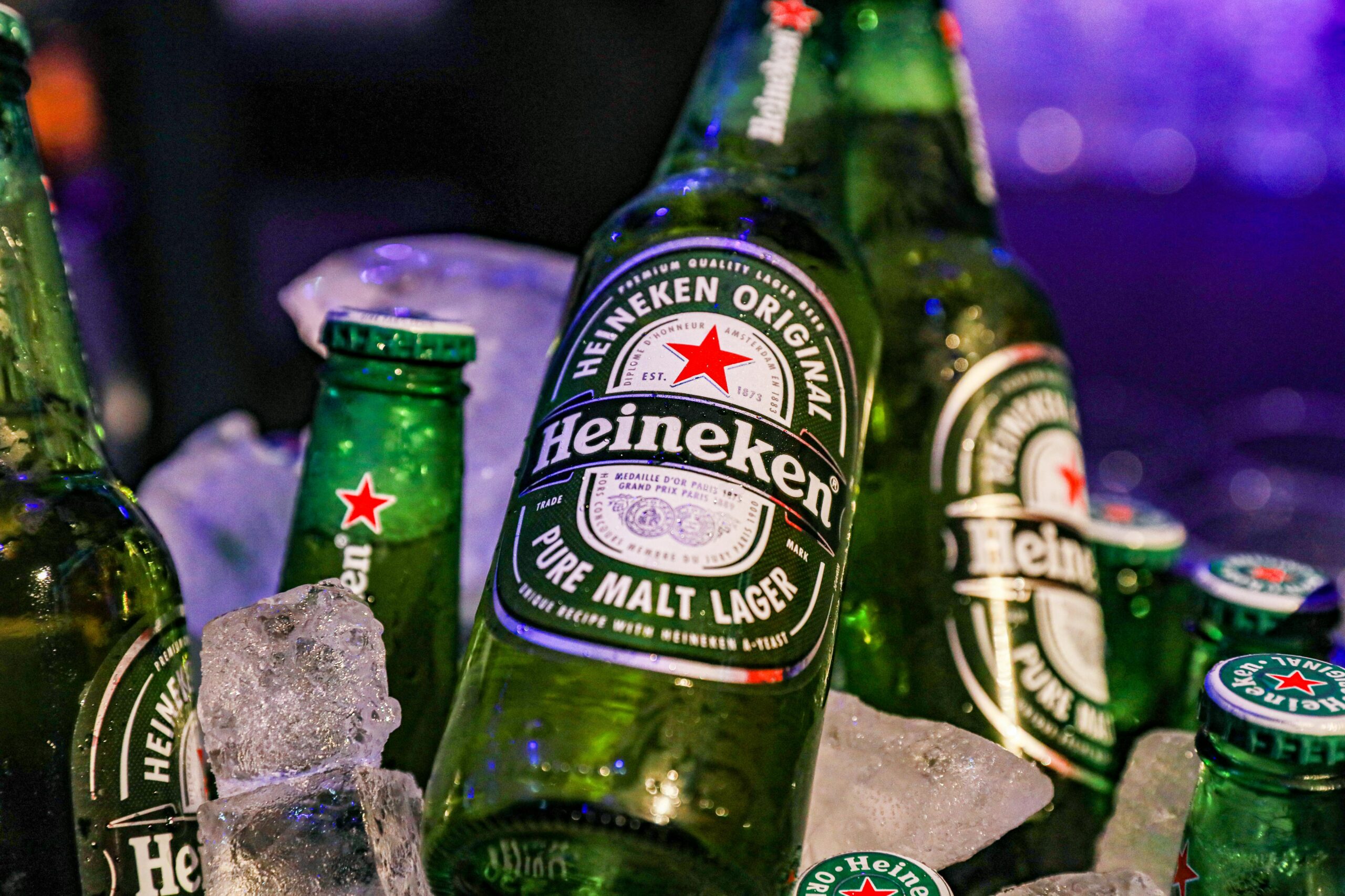 Closeup of green glass bottles of cold famous lager beer against blurred background with neon lights during party