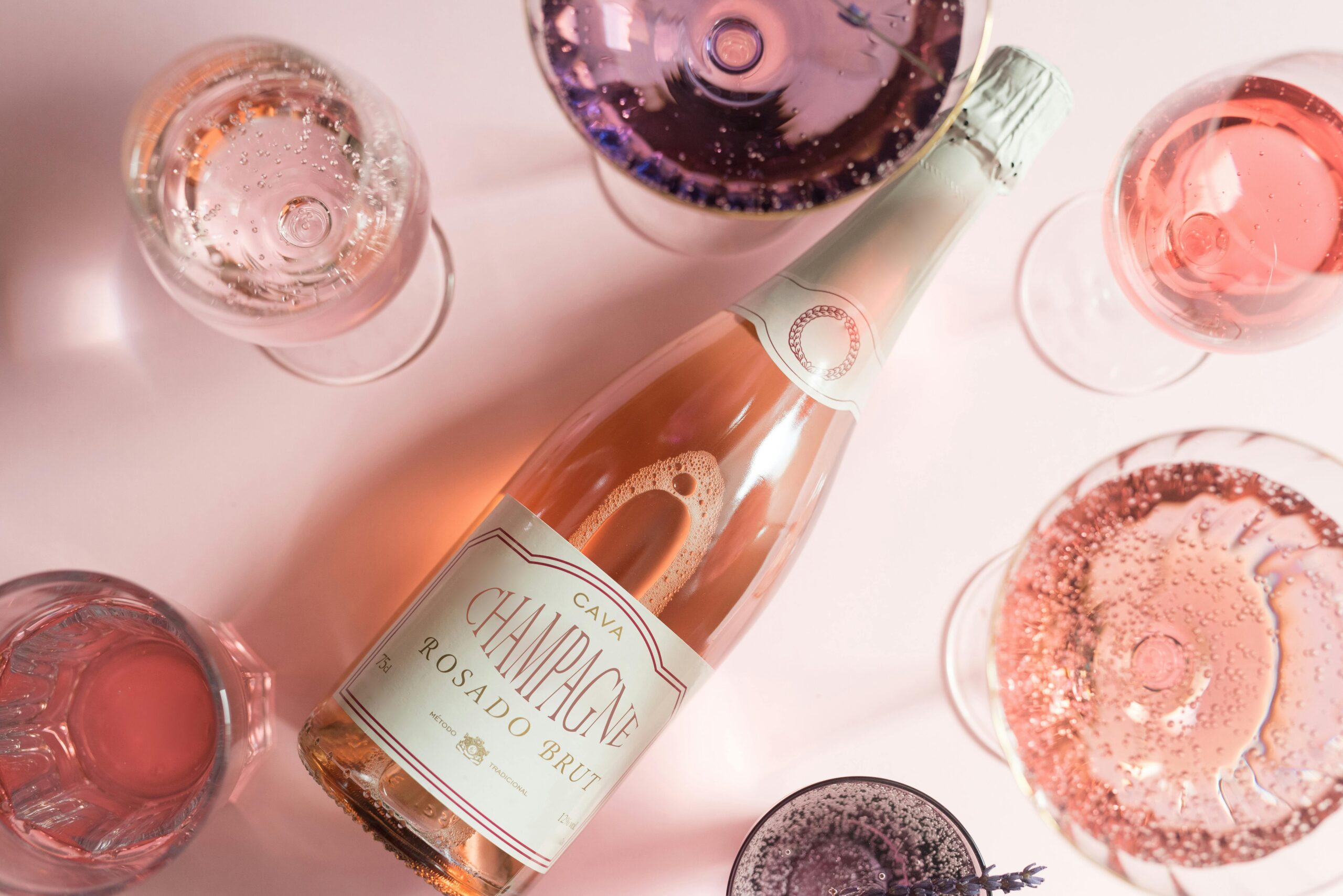 Flat lay of rosé champagne bottle with various glasses on a light pink background.